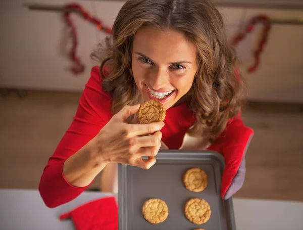 Smiling young housewife tasting cookie from pan with christmas cookies — Stock Photo, Image