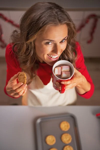 Feliz joven ama de casa beber chocolate caliente y comer galleta —  Fotos de Stock