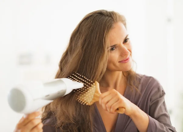 Happy woman brushing and blow drying hair in bathroom — Stock Photo, Image