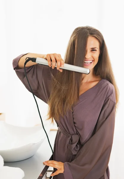 Smiling young woman straightening hair with straightener — Stock Photo, Image