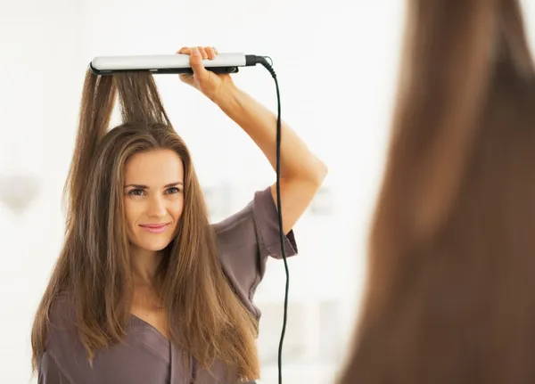 Portrait of woman straightening hair with straightener — Stock Photo, Image