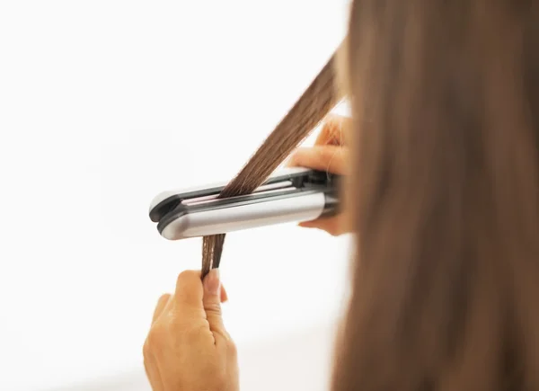 Nahaufnahme einer Frau, die ihr Haar mit einem Glätteisen glättet — Stockfoto