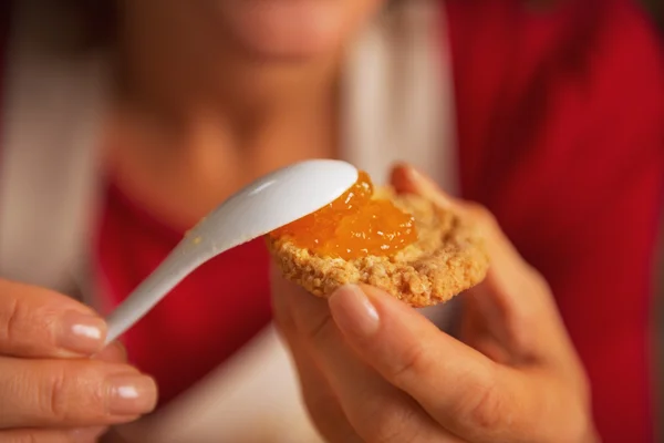 Primer plano de la mujer joven poniendo mermelada de naranja en la galleta — Foto de Stock