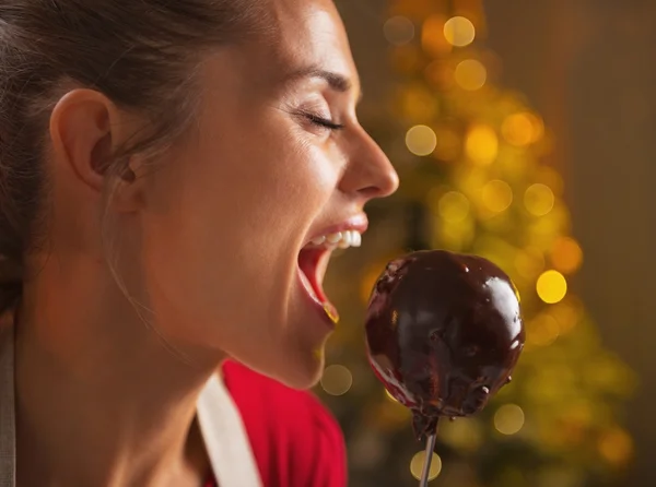 Glückliche junge Hausfrau isst Apfel in Schokoglasur — Stockfoto