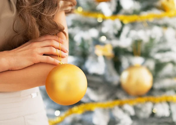 Bola de Natal na mão da jovem mulher em pé perto da árvore de Natal — Fotografia de Stock