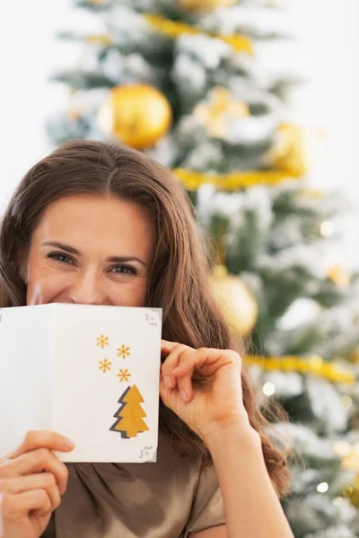 Happy young woman hiding behind christmas postcard — Stock Photo, Image