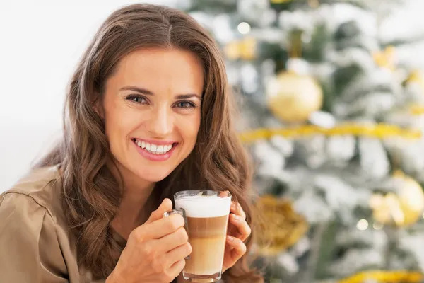 Jonge vrouw met latte macchiato voor kerstboom — Stockfoto
