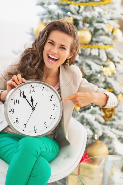 Mujer joven sonriente señalando el reloj frente al árbol de Navidad — Foto de Stock