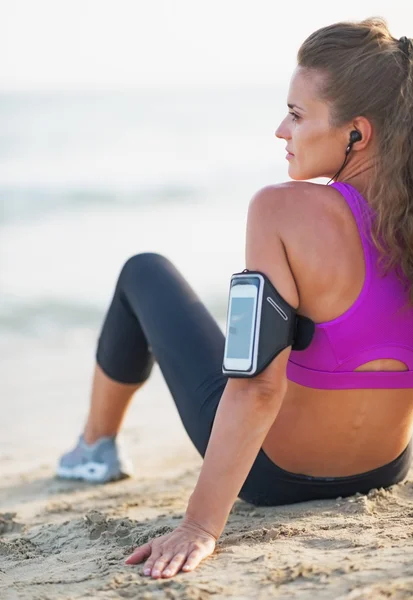 Mujer joven fitness en auriculares sentados en la playa — Foto de Stock