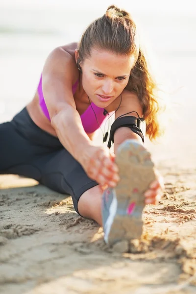 Фитнес молодая женщина в наушниках растягивается на пляже — стоковое фото