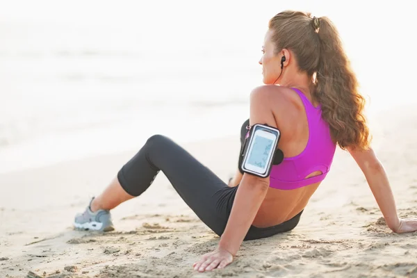 Fitness young woman in headphones sitting on beach — Stock Photo, Image