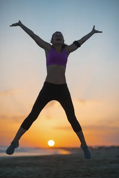 健身年轻女子在黄昏时在海滩上跳跃的剪影 — 图库照片