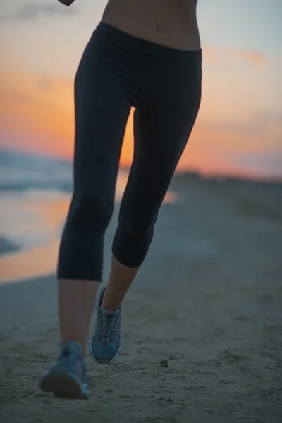 Primo piano sulla donna fitness che corre sulla spiaggia al tramonto — Foto Stock