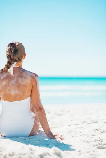 Junge Frau im Badeanzug sitzt am Sandstrand — Stockfoto