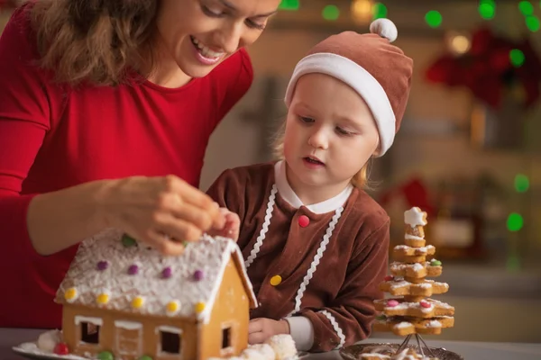 Mor och barn dekorera jul cookie hus i köket — Stockfoto