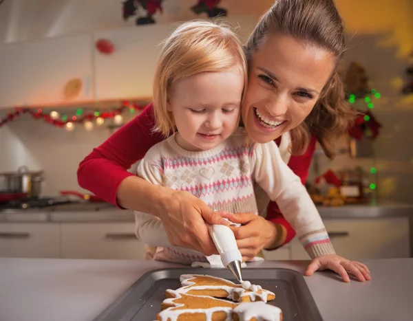 Mor och barn dekorera hemlagade pepparkakor med glasyr — Stockfoto