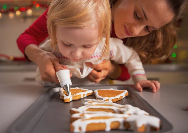 Ребенок помогает матери украсить домашнее рождественское печенье глазурью — стоковое фото