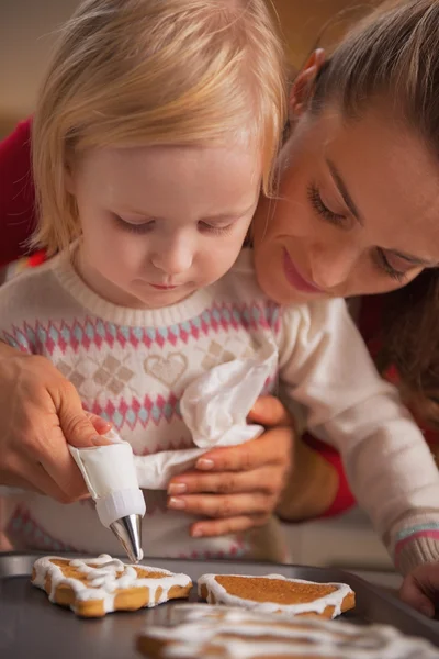 Mor och barn dekorera hemlagade pepparkakor med glasyr — Stockfoto