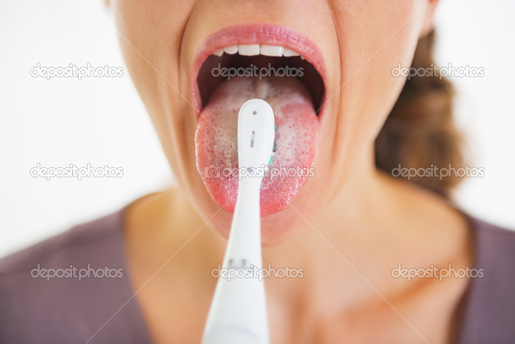 Closeup on young woman cleaning tongue using toothbrush