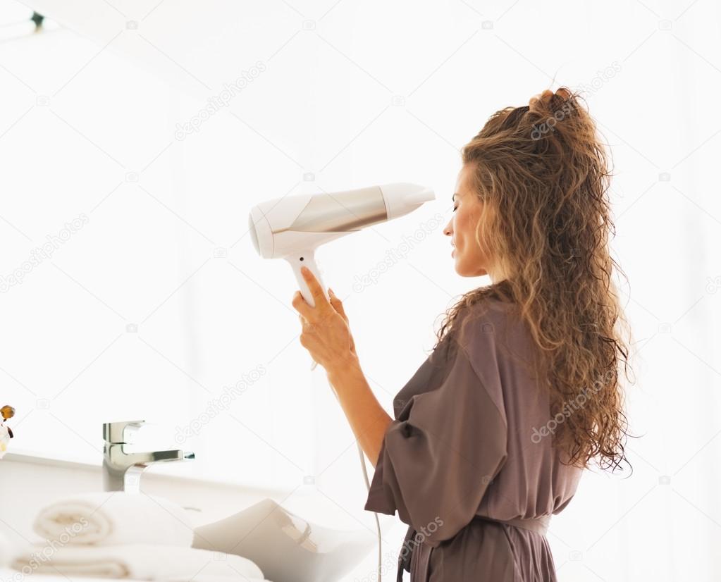 Young woman blow drying hair in bathroom