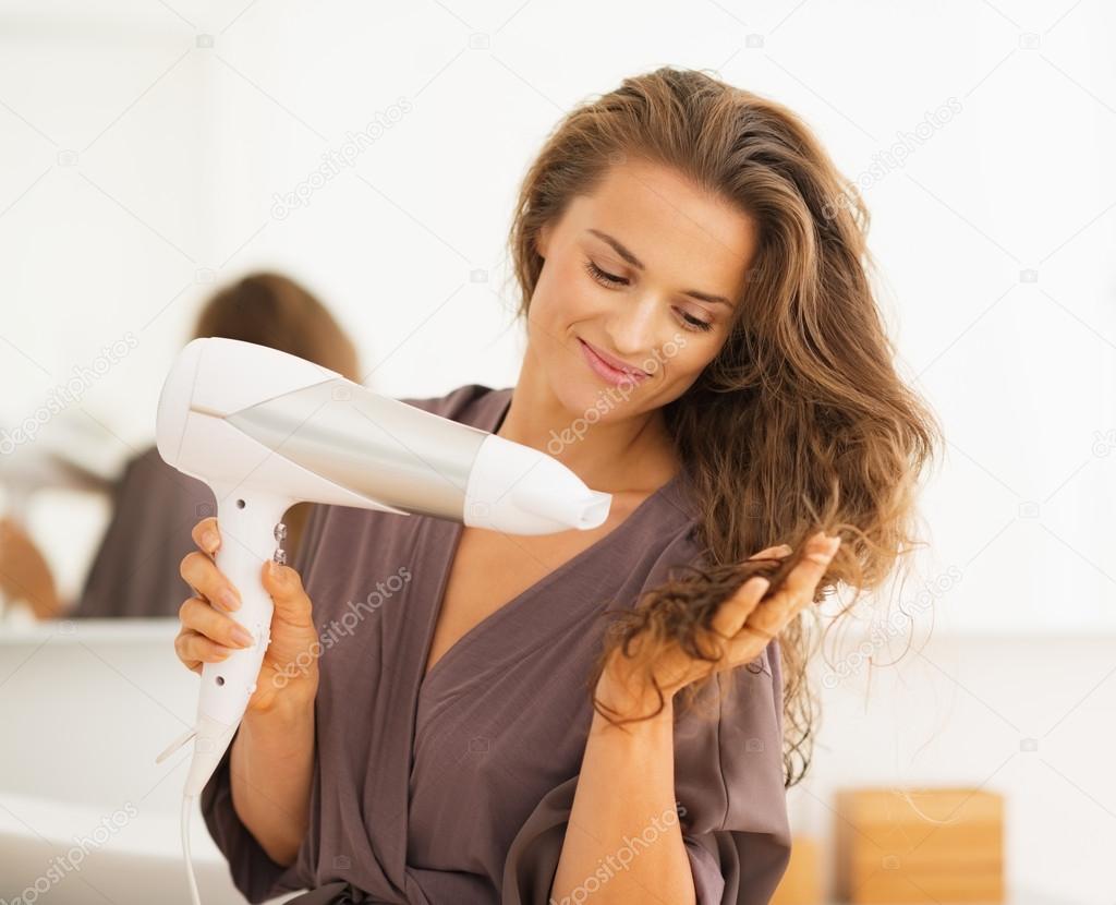 Happy young woman blow drying hair in bathroom