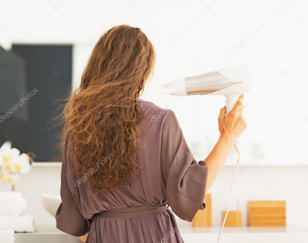 Young woman blow drying hair in bathroom