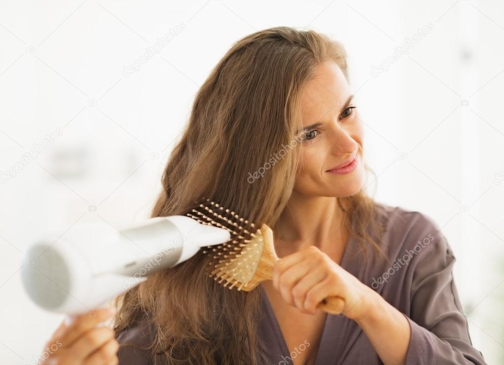 Happy woman brushing and blow drying hair in bathroom