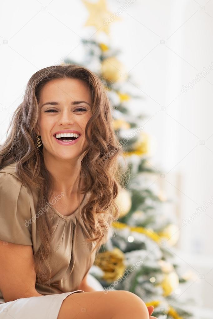 Smiling young woman sitting in front of christmas tree