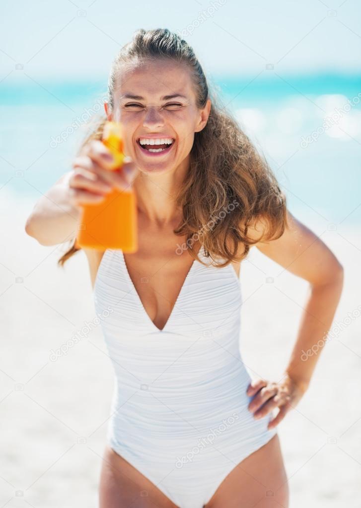 Happy young woman aiming bottle of sun block creme in camera