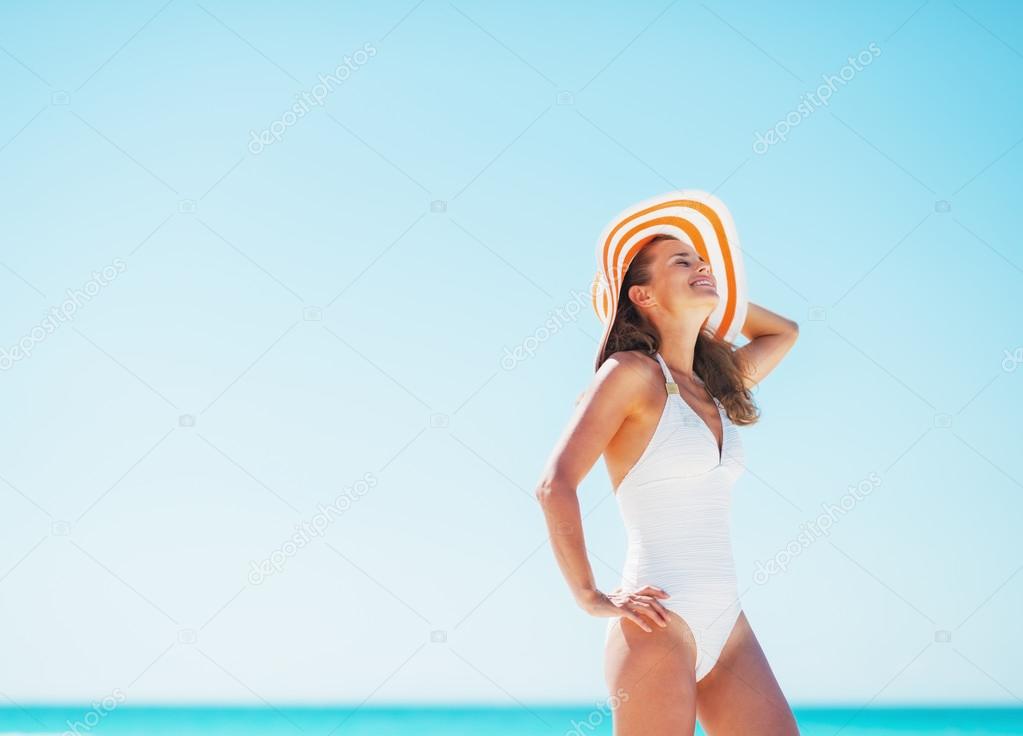 Happy young woman in swimsuit and beach hat relaxing on beach