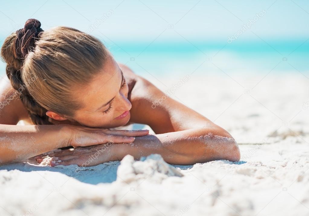 Happy young woman in swimsuit relaxing while laying on sandy bea