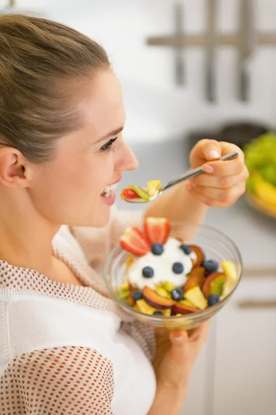 Jovem dona de casa feliz comendo salada de frutas frescas — Fotografia de Stock