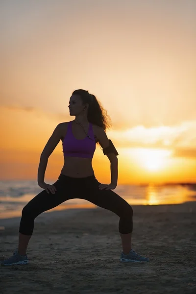 Silueta fitness mladá žena při cvičení na pláži za soumraku — Stock fotografie