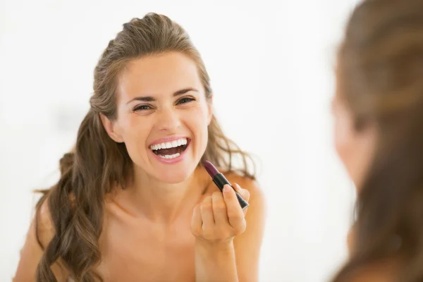 Gelukkig jonge vrouw toepassing lippenstift in badkamer — Stockfoto