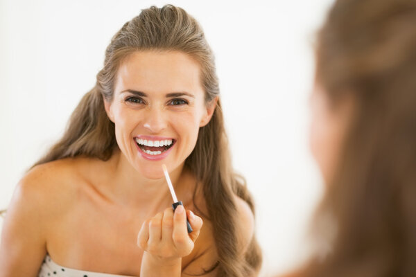 Happy young woman applying lip gloss in bathroom