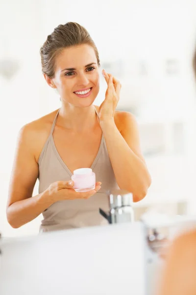 Souriant jeune femme appliquant la crème dans la salle de bain — Photo