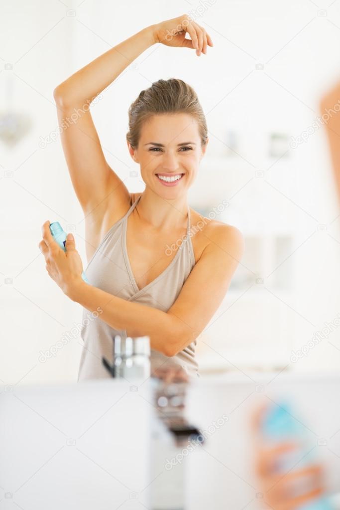 Smiling young woman applying deodorant on underarm