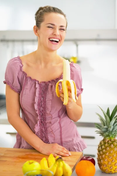 Sonriente joven comiendo plátano en la cocina — Foto de Stock
