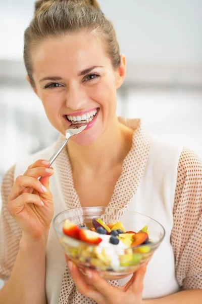 Jovem dona de casa feliz comendo salada de frutas frescas — Fotografia de Stock