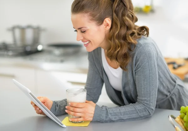 Mujer joven feliz con smoothie usando tableta PC en la cocina —  Fotos de Stock