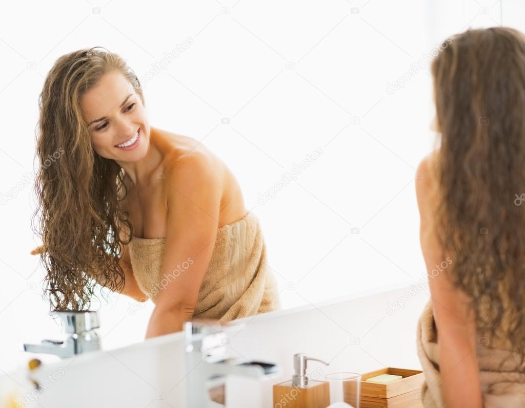 Smiling young woman sitting with wet hair in bathroom and lookin