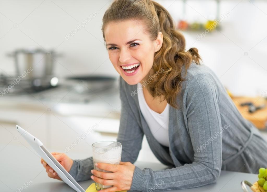 Smiling young woman with smoothie using tablet pc in kitchen