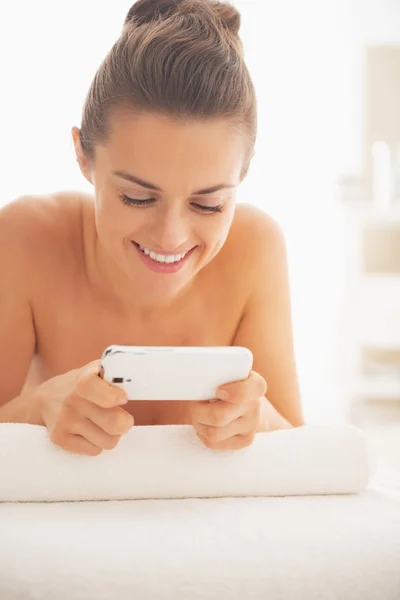 Portrait of happy young woman writing sms while laying on massage table — Stock Photo, Image