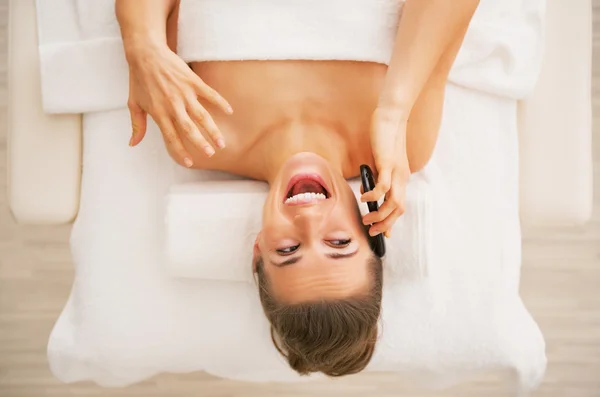 Happy young woman laying on massage table and talking cell phone — Stock Photo, Image