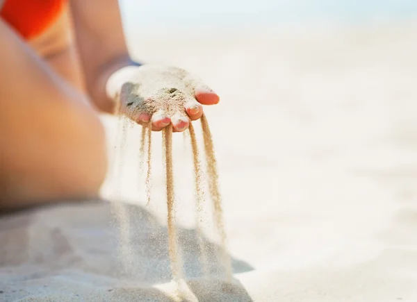 Крупный план молодой женщины, сидящей на пляже и играющей с песком — стоковое фото