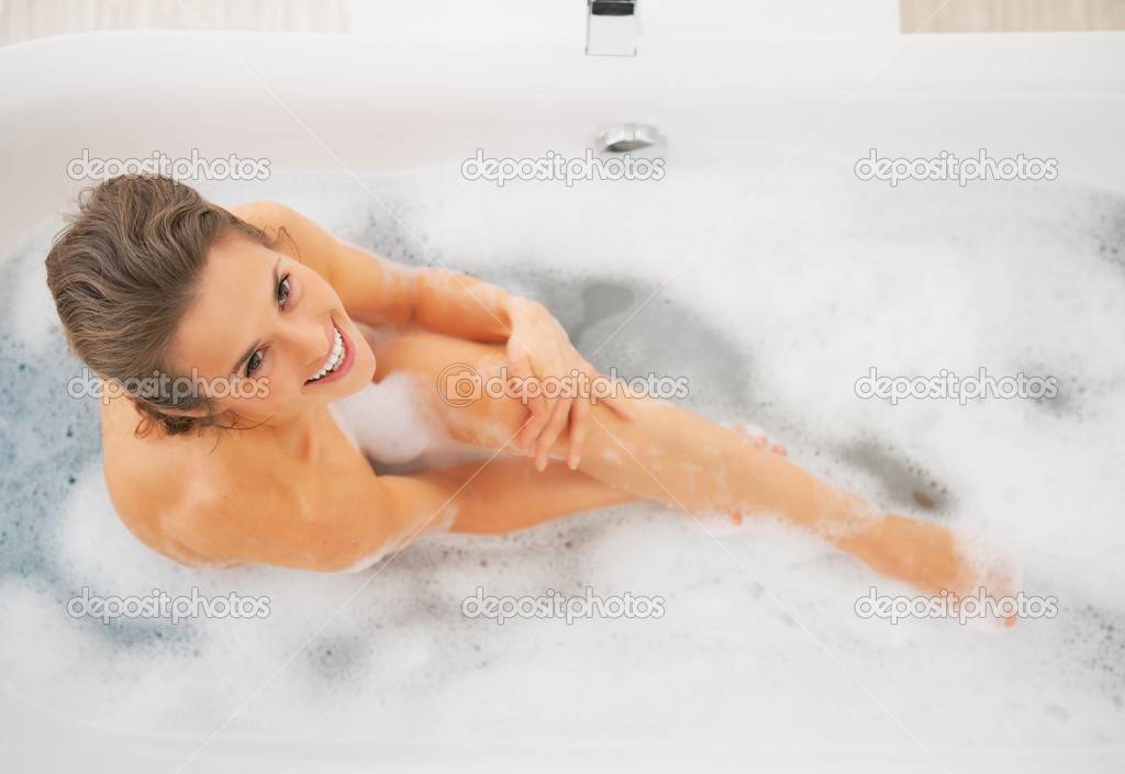 Happy young woman washing in bathtub