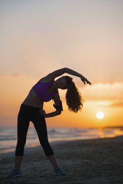 gün batımında sahilde uzanan fitness genç kadın silüeti