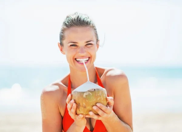 Glückliche junge Frau trinkt Kokosmilch am Strand — Stockfoto