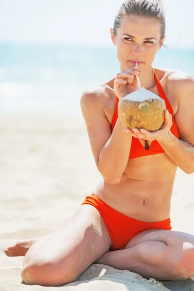 Ευτυχής νεαρή γυναίκα που πίνει γάλα καρύδας στην παραλία — Φωτογραφία Αρχείου