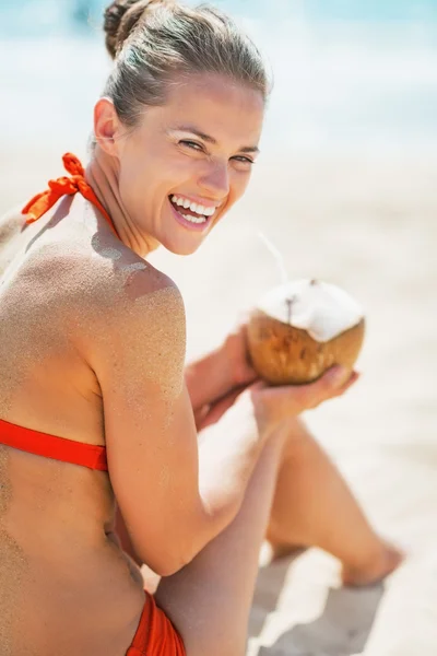 Lächelnde junge Frau sitzt mit Kokosnuss am Strand — Stockfoto